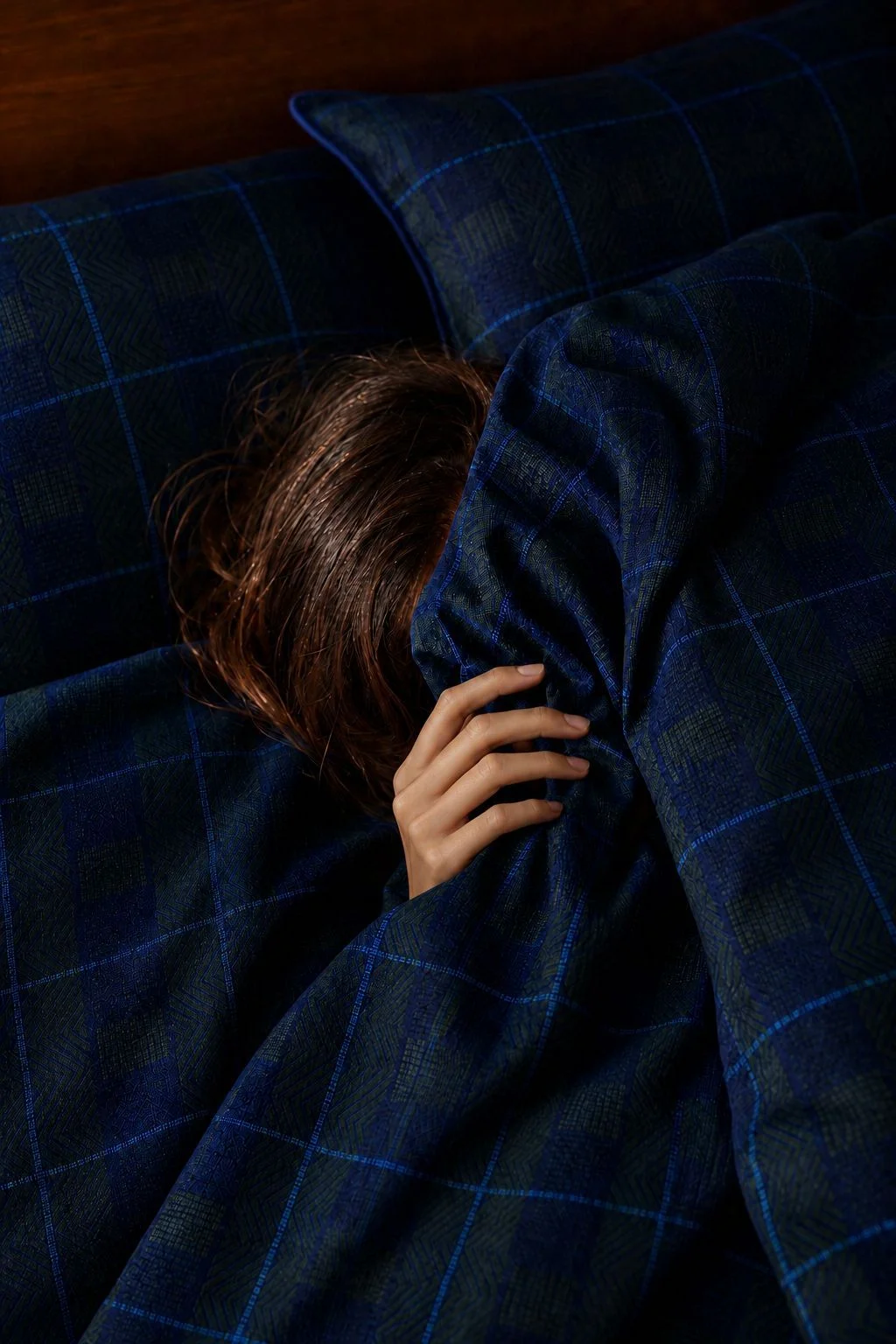 Wilmotte source still: a face hidden beneath the duvet, with a hand and strands of hair visible.