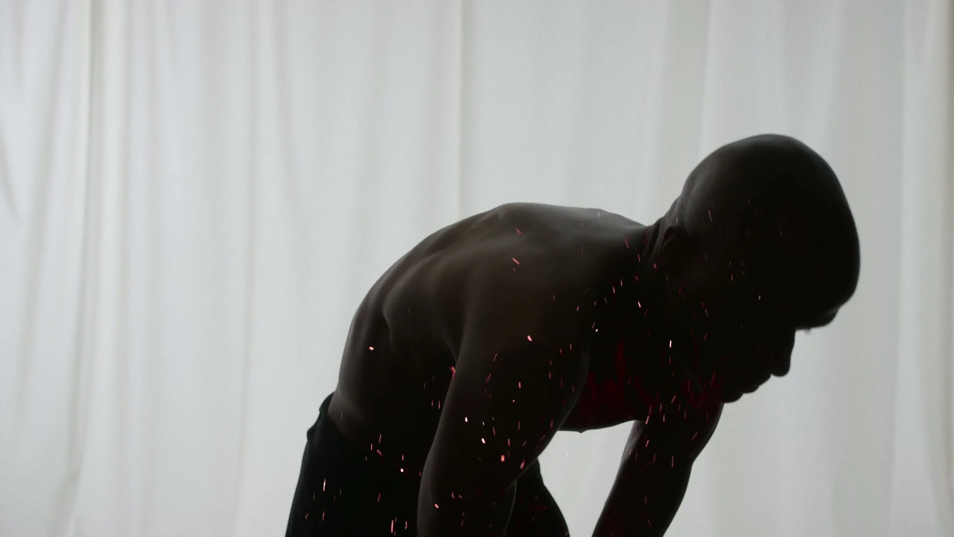 Red sparks cross a torso in front of the curtains.